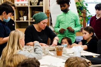 Students gathering around watching Rebekah work with clay