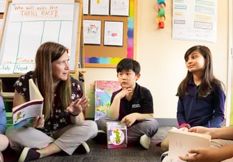 2nd grade teacher explains a book while three children listen