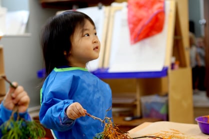 Toddler with paint apron on holding branches