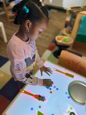 Student in pink sweatshirt counts out dots on light table