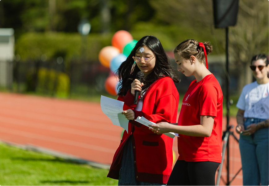 Two Female Students Speaking into a Microphone on a Track