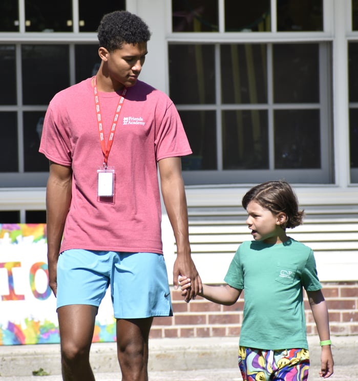 Boy counselor with pink shirt holding hand of camper in green T-shirt