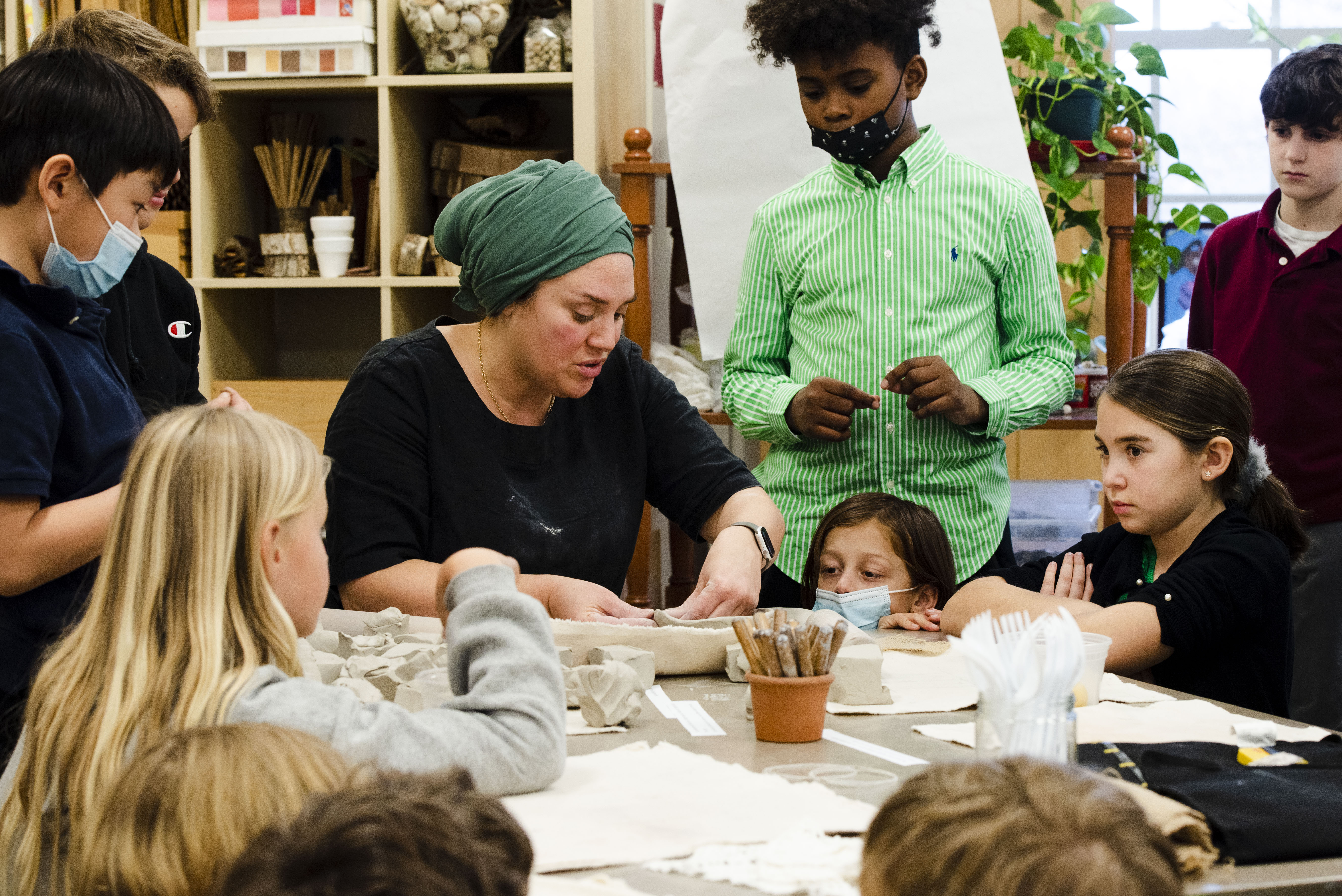 Students gathering around watching Rebekah work with clay