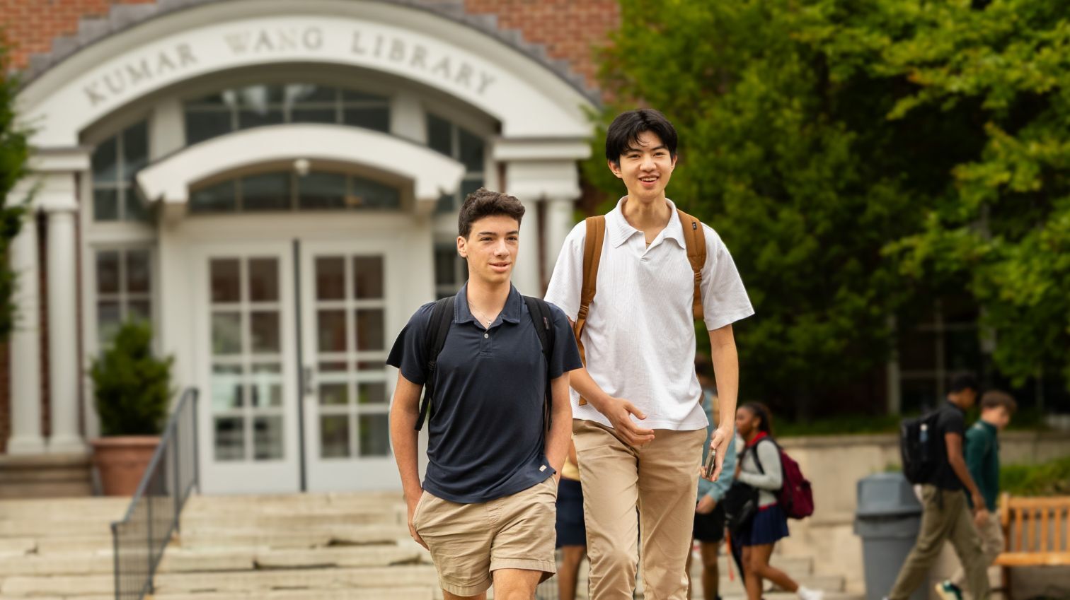 Two students with backpacks walk in front of a building labeled 